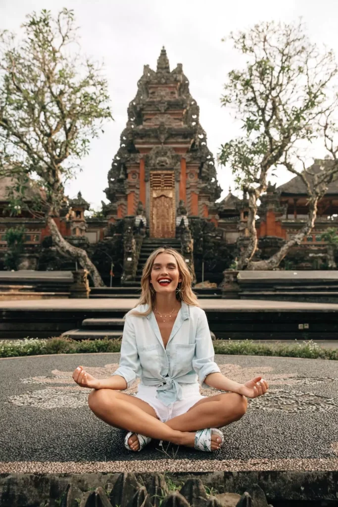 Bali Ai - 
A female foreign tourist is taking a photo with a temple in Bali in the background, looking happy and enjoying herself.