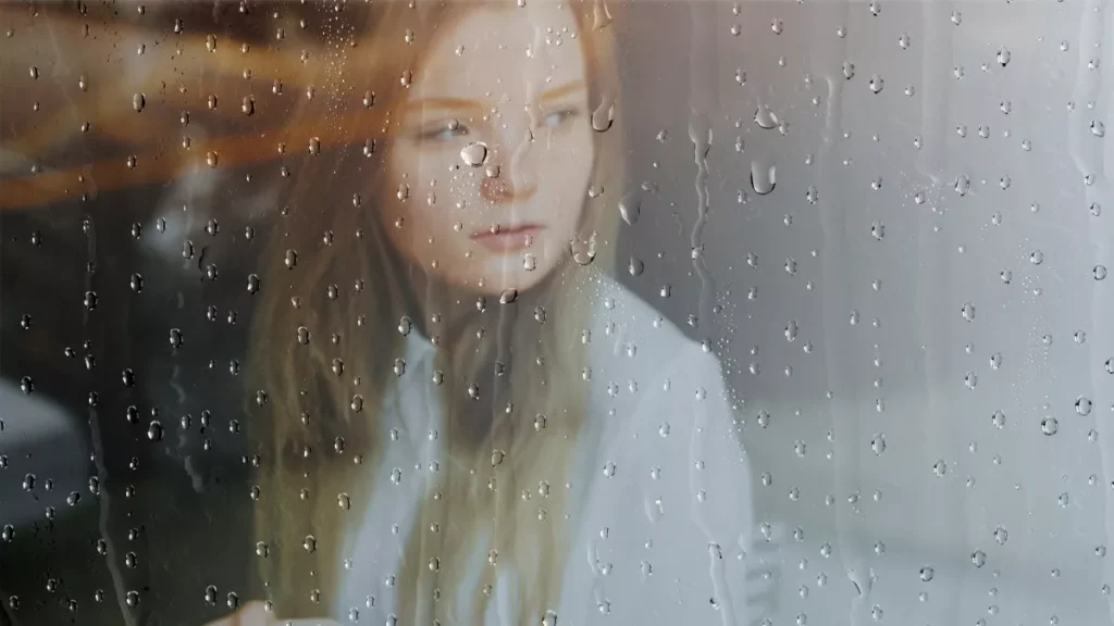 Wanita menatap keluar jendela kaca saat Hujan