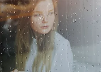 Wanita menatap keluar jendela kaca saat Hujan