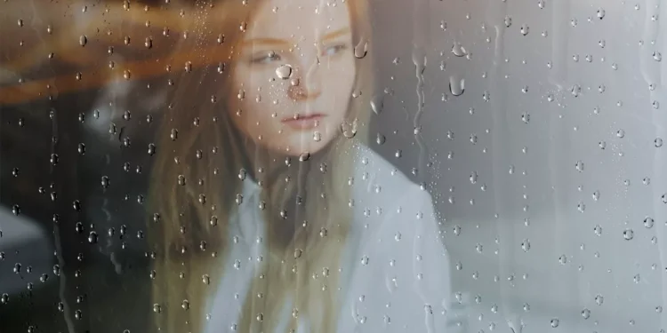 Wanita menatap keluar jendela kaca saat Hujan