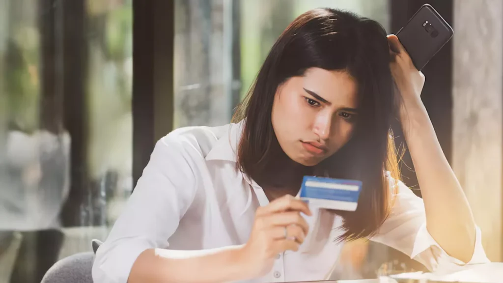 Photo of an Asian woman looking confused while holding her credit card (Source: Freepik)