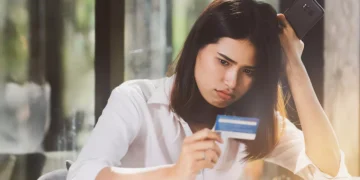 Photo of an Asian woman looking confused while holding her credit card (Source: Freepik)