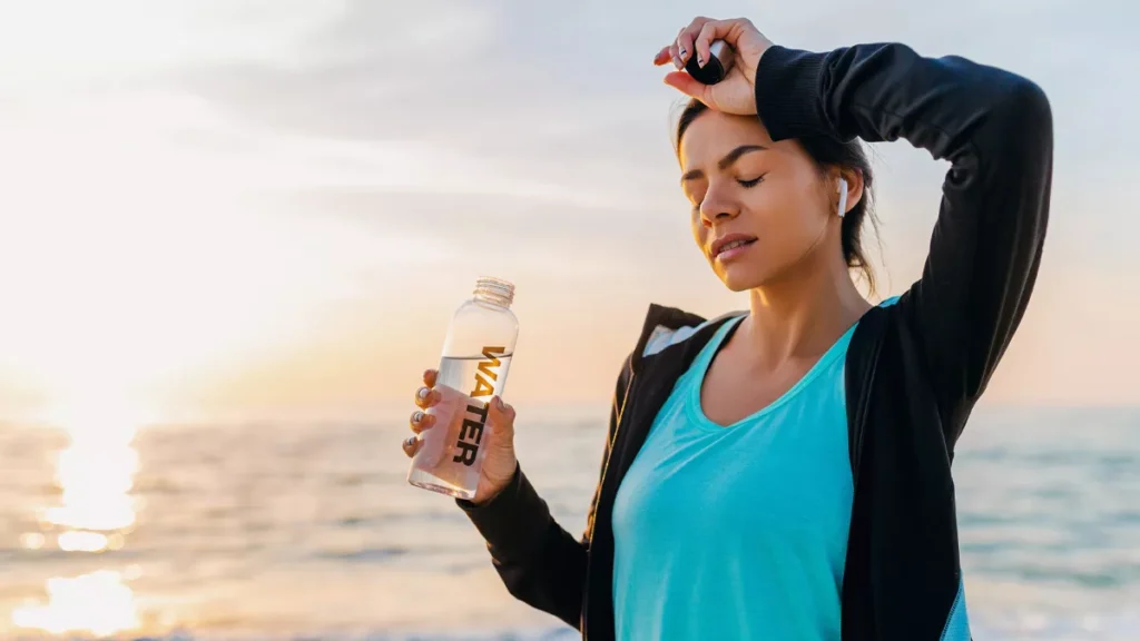 Why Bali Feels So Hot Right Now: BMKG Explains the Science Behind the Heat 38 Photo of a woman holding a bottle of mineral water on the beach and feeling the heat of Bali (Hey Bali)