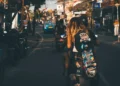 Bali's Most Famous Destinations Aren't Losing Their Magic. They're Becoming Victims of Their Own Success. 49 Photo of the atmosphere on a street in Bali shows a Caucasian woman riding a motorbike while carrying a skateboard.