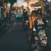 Bali's Most Famous Destinations Aren't Losing Their Magic. They're Becoming Victims of Their Own Success. 45 Photo of the atmosphere on a street in Bali shows a Caucasian woman riding a motorbike while carrying a skateboard.