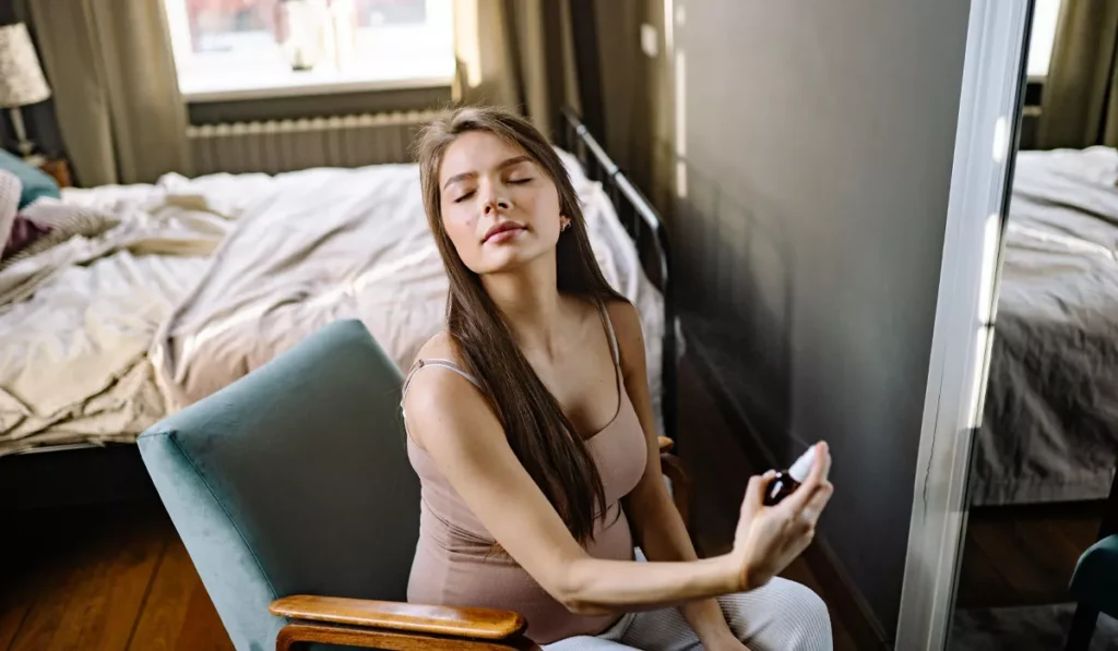 Why Doesn't Perfume Last in Bali? Here's the Science (And How to Make It Last Longer) 40 Woman applying perfume indoors before exploring Bali in warm tropical weather.