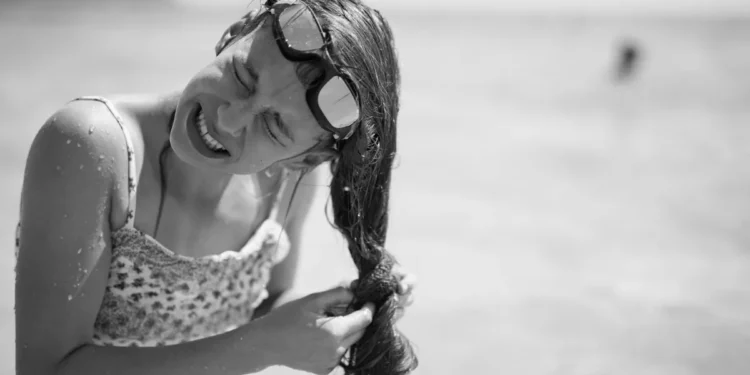 Woman struggling with tangled sticky hair after swimming in the ocean without rinsing off salt water.