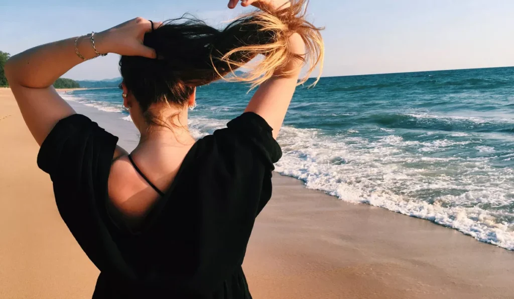 Why Does Salt Water Make Your Hair Feel Sticky? Here's the Science, and What It Means After a Day at a Bali Beach 38 Traveler tying up sticky salt water hair after walking along a Bali beach following an ocean swim.