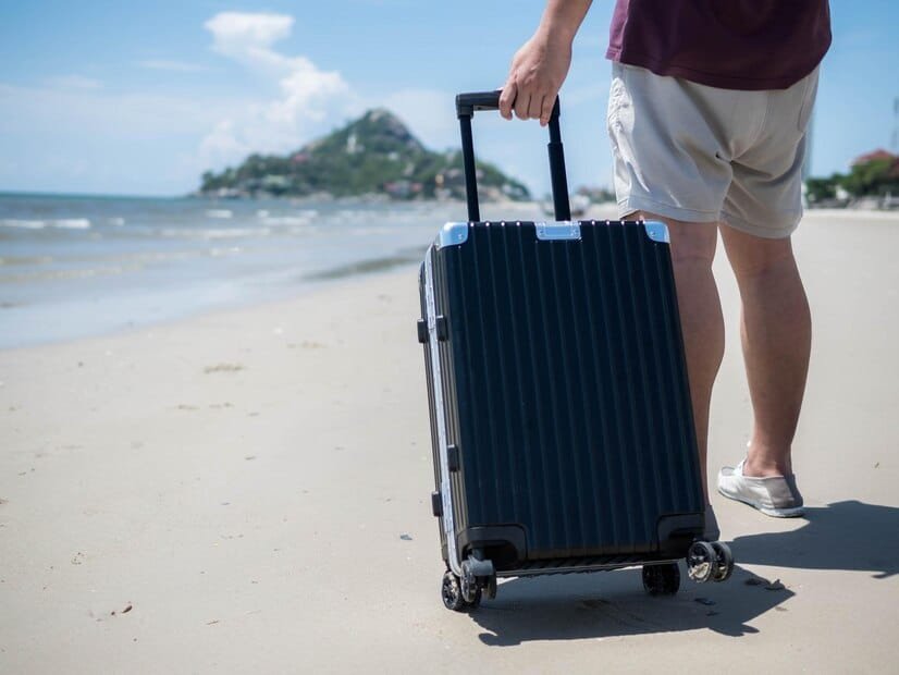 Photo of a traveler on the beach sand holding his black suitcase - Cheap Bag Storage in Kuta