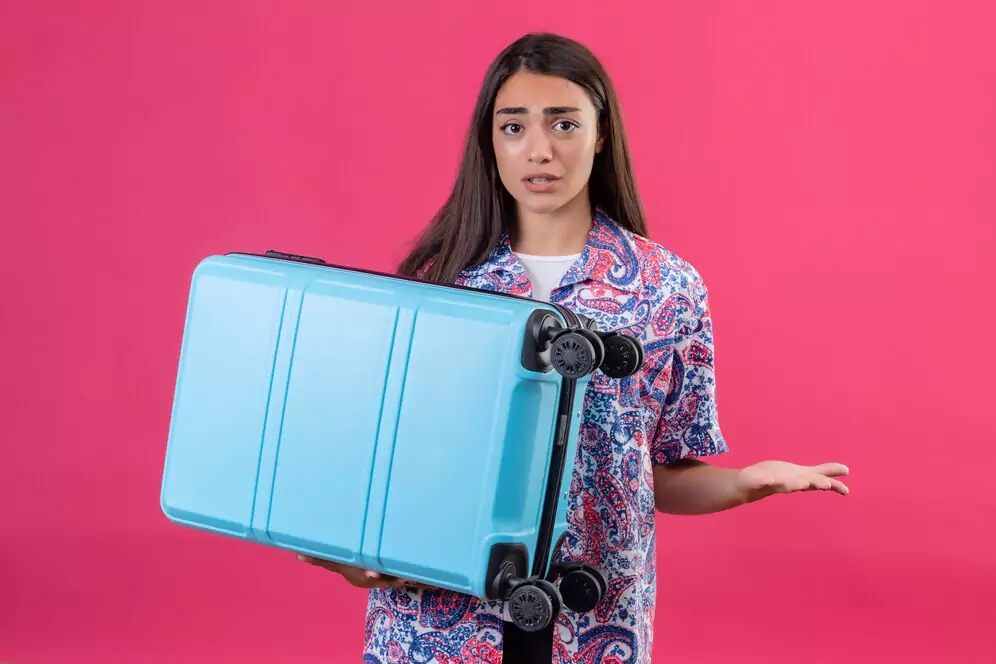 a Caucasian woman holds a blue suitcase in one hand and the other hand seems to be asking where is the best place for luggage storage in Bali.