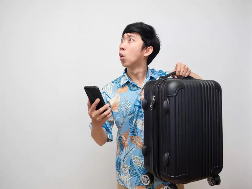 a man holding a cell phone and a suitcase looks confused about how to find the best luggage storage in bali