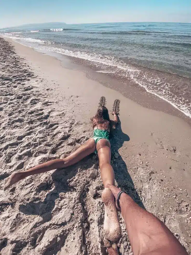 Bali Survival Guide - Cute photo of a female tourist sleeping on the sand of Balangan beach and her legs are being pulled by her partner with a beautiful beach background.