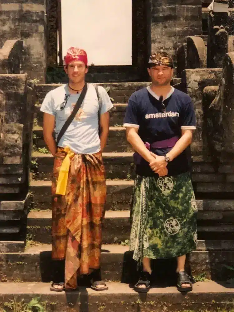 An old photo of two Caucasian men from the Netherlands wearing Balinese traditional clothes and taking a photo with a temple background