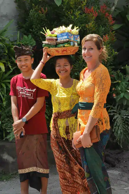 Caucasian woman wearing Balinese traditional clothes mingles with local people after praying at a temple - Om Swastiastu meaning