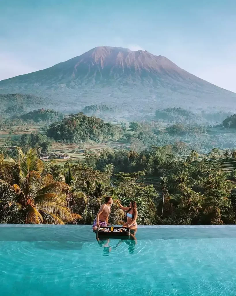 A couple of tourists are having breakfast by the pool with a view of Mount Batur. - Private Bali Tours
