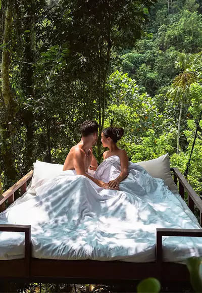 A pair of foreign tourists pose on a bed swing in Ubud with the forest as a backdrop.