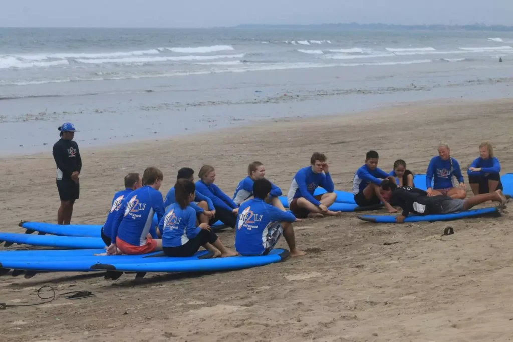 A group of tourists are listening to a coach explaining how to surf on Legian Beach in Bali before heading out to sea.