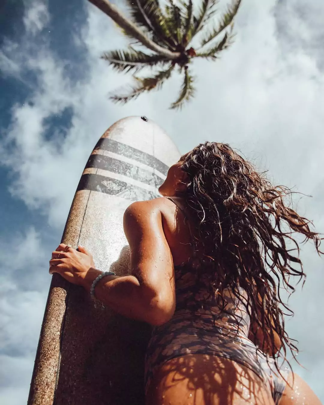 A female tourist poses while holding a surfboard.