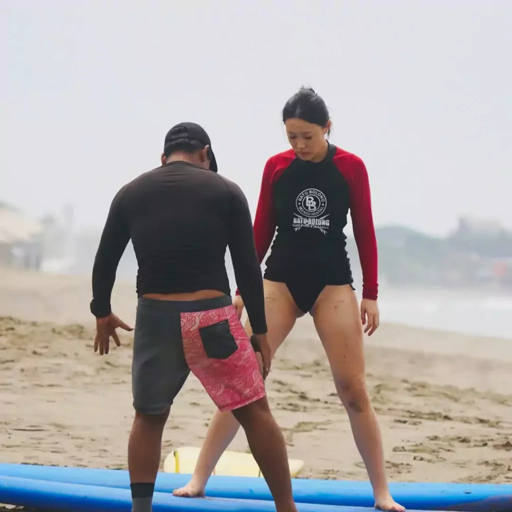 An instructor is giving a basic surfing lesson to a Chinese tourist at Canggu Beach, Bali.
