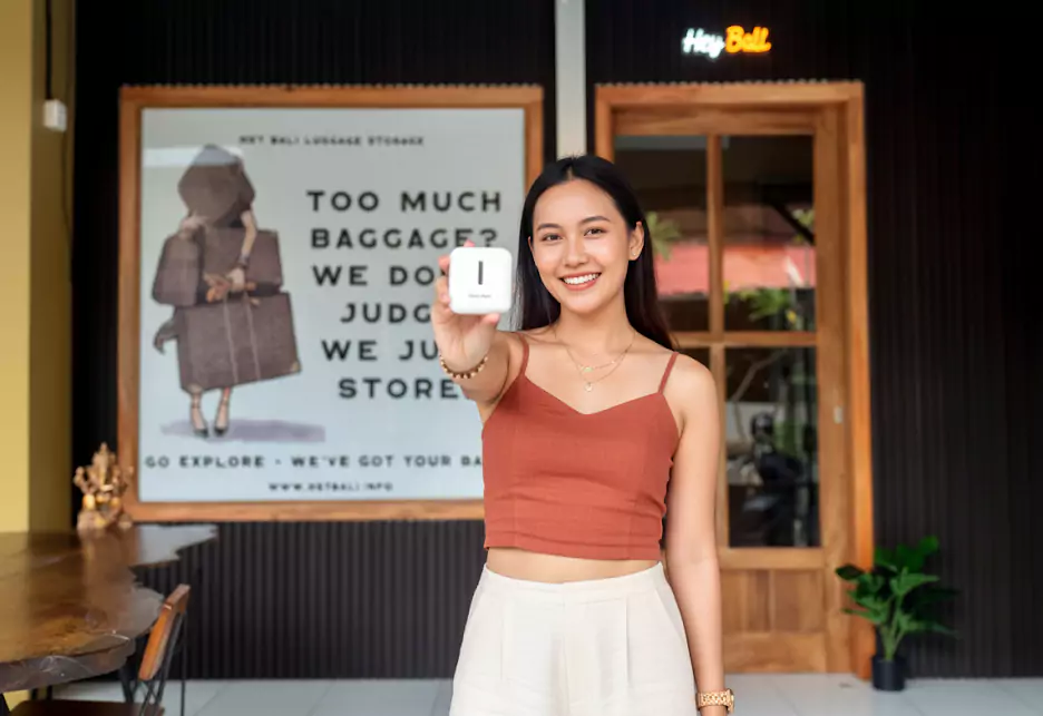 A photo of a happy Singaporean woman posing in front of the Hey Bali office while showing off the free adapter she got from Hey Bali.