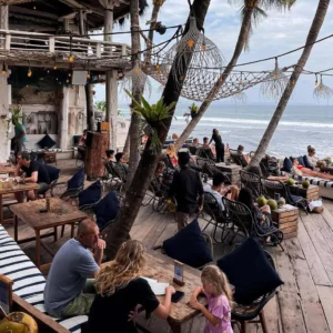 Beachfront café in Canggu, Bali with people enjoying food and ocean views — a popular stop after traveling from Bali Airport to Canggu.