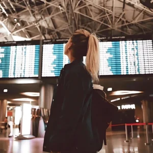photo of a woman at an airport looking at the plane departure schedule board