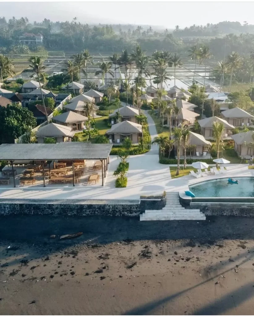Drone shot of a serene Seaside Glamping in Bali property next to the ocean, showing the pool area and surrounding greenery.