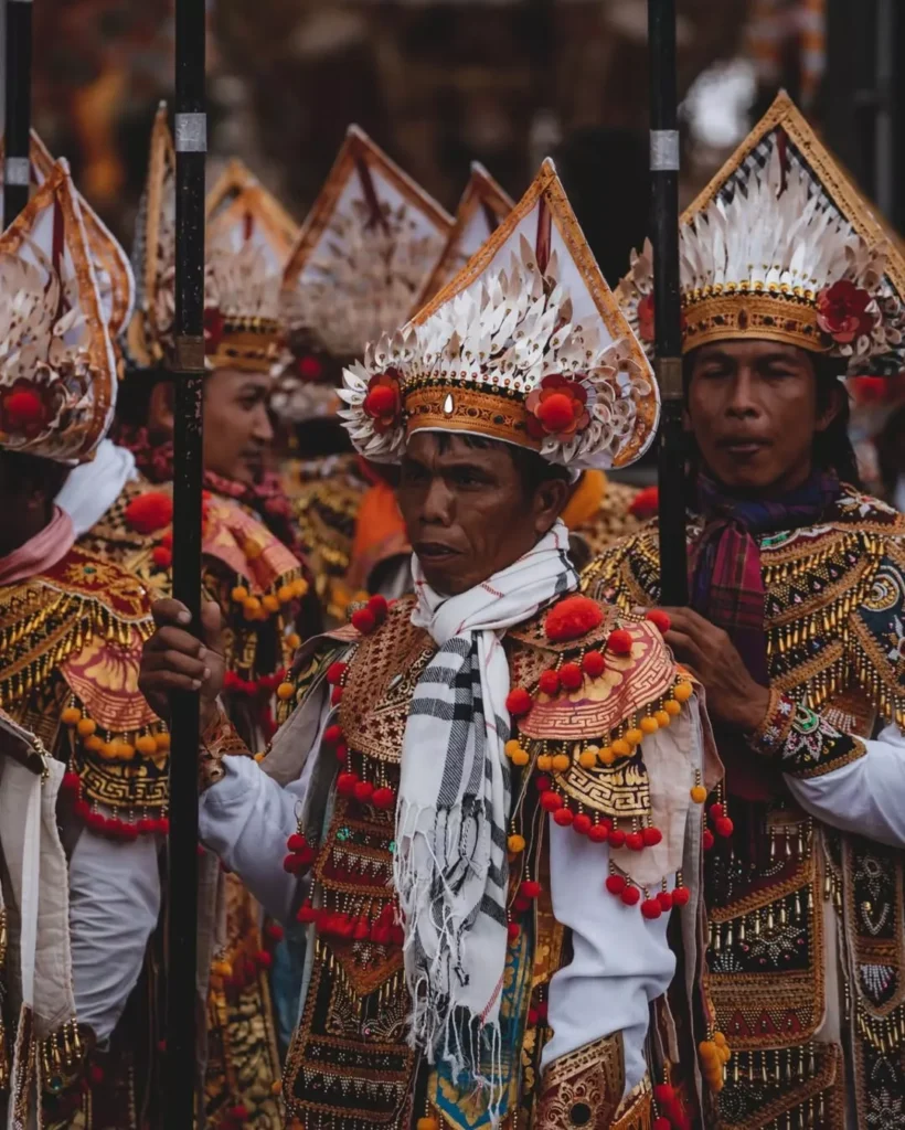 Balinese men in full traditional ceremonial dress and elaborate headdresses, participating in a cultural procession. Alt: The question is Bali overrated ?overlooks the profound spiritual significance and cultural depth of ceremonies like this.