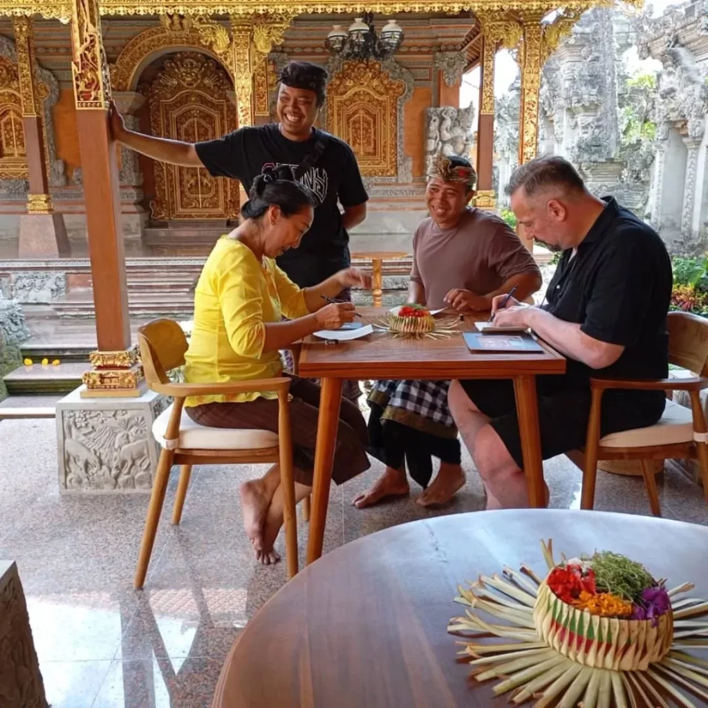 A smiling man wearing sunglasses, a white shirt, and khaki shorts, sitting cross-legged in a narrow, immersive tunnel made of countless colorful, stacked Balinese handcrafted pottery vases and pots, showcasing the vibrant artistic scene.