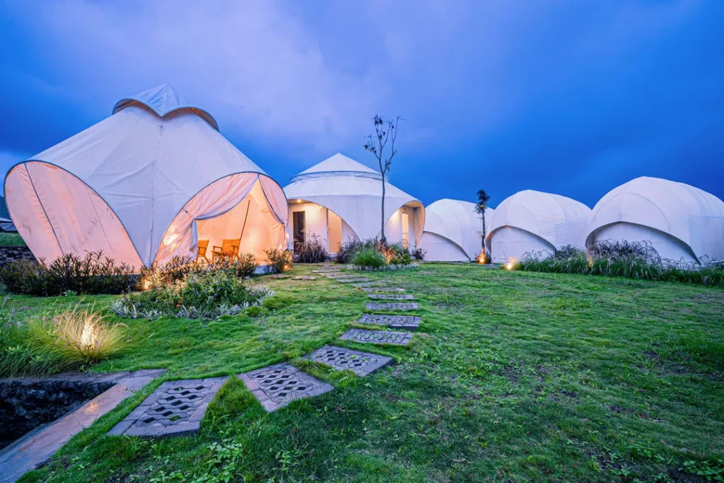 Beautiful night shot of modern white tents at a Luxury Glamping Bali resort, glowing softly amidst green grass.