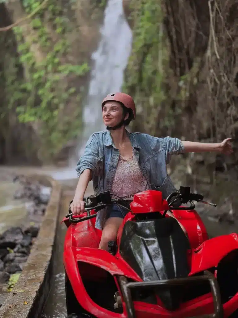 Woman on a red ATV helmet enjoying an adventure through Bali's jungle and waterfall area. Engaging in direct action like this is the definitive cure for the lack of curiosity that results in the question 'is Bali boring?'