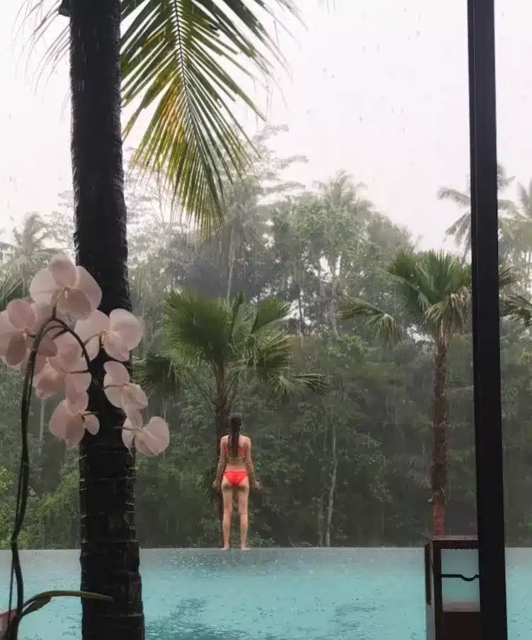 A female tourist takes a photo by the pool with a forest background in Ubud, Bali.